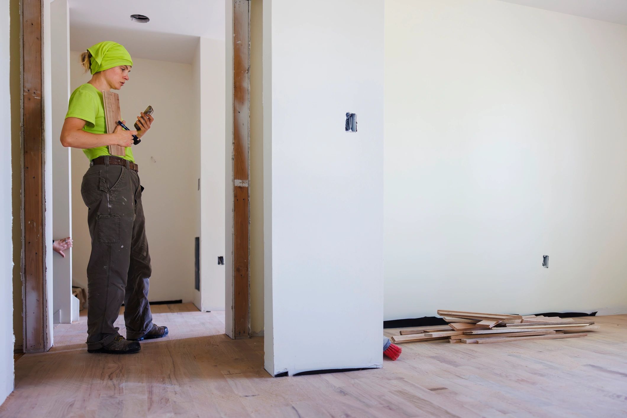 Contractor checking smartphone while standing in doorway. Renovation project with unfinished drywall and exposed electrical outlets.